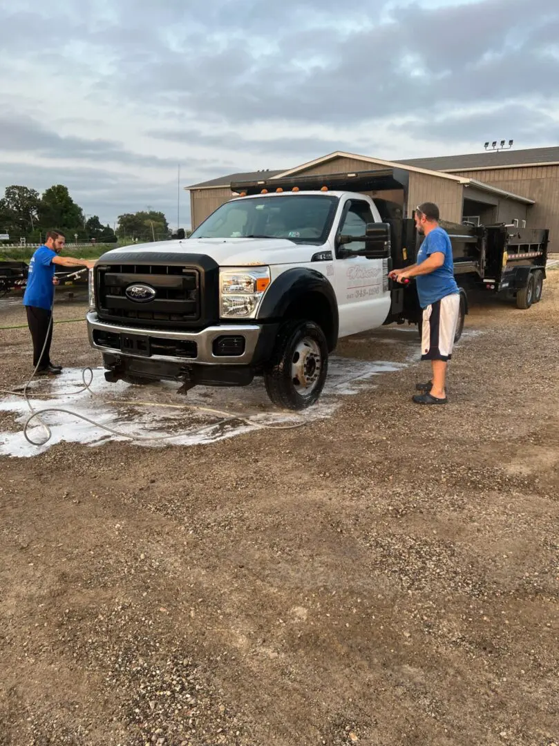 A man and woman washing a truck in the dirt.